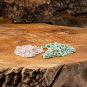 Zwei Haufen getrommelter Edelsteine, Rosenquarz und Amazonit, liegen auf einer rustikalen Holzoberfläche zur Wasserenergetisierung.
