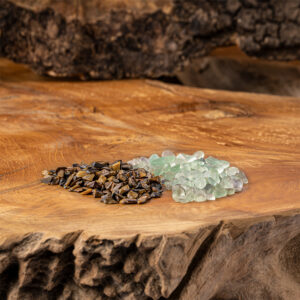 Zwei kleine Haufen getrommelter Edelsteine, Fluorit und Tigerauge, liegen auf einer rustikalen Holzoberfläche.