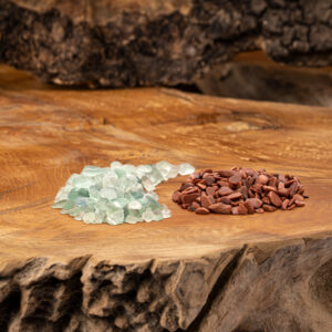 Zwei Haufen naturbelassener Wassersteine, hellgrüner Fluorit und rotbrauner Goldfluss, auf einer rustikalen Holzoberfläche.