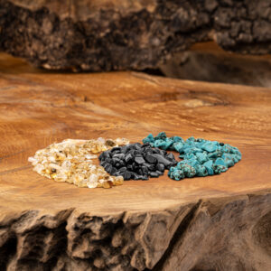 Drei verschiedene Edelsteinmischungen – Goldener Beryll, Turmalin und Türkis – liegen auf einer rustikalen Holzoberfläche.