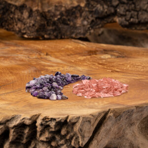 Zwei sorgfältig arrangierte Kristallstein-Mischungen, eine in violetten und eine in rötlichen Tönen, liegen auf einer rustikalen Holzoberfläche.