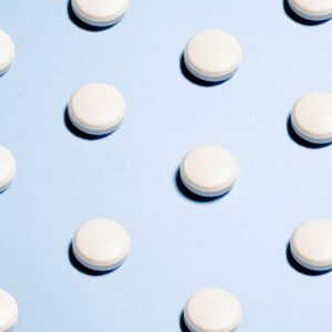Weiße Tabletten auf blauem Hintergrund als Symbol für Hausmittel gegen Kalk.