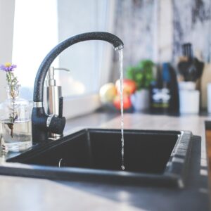 Klares Wasser fließt aus einem modernen Wasserhahn in ein Spülbecken, Symbol für sauberes Trinkwasser.