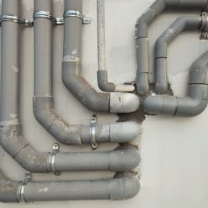 Komplexes System aus alten, grauen Wasserleitungen, die an einer Wand montiert sind.