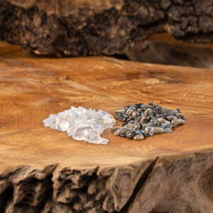 Zwei kleine Haufen getrommelter Edelsteine, heller Mondstein und dunkler Labradorit, liegen auf einer rustikalen Holzscheibe.