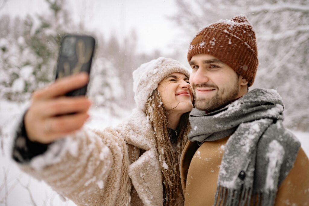 Ein glückliches Paar genießt die gemeinsame Zeit bei einem winterlichen Ausflug im Schnee und macht ein Selfie.