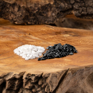 Zwei Haufen mit schwarzen Turmalin- und weißen Milchopal-Edelsteinen auf einer rustikalen Holzoberfläche.