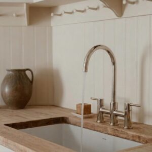 Eine helle Küche mit einer Arbeitsplatte aus Holz, in der klares Wasser aus einem modernen Wasserhahn in ein weißes Spülbecken fließt.