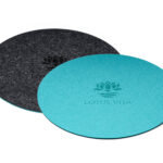 Ein runder Filz-Untersetzer in Türkis und Anthrazit, der beidseitig verwendbar ist und das Lotus Vita Logo zeigt.